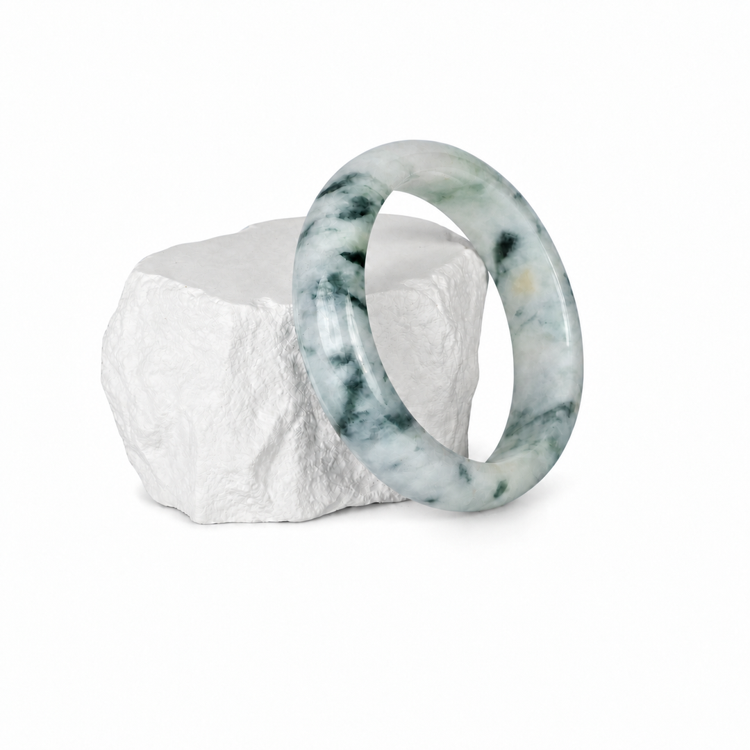 White and grey jadeite bangle displayed on a white stone