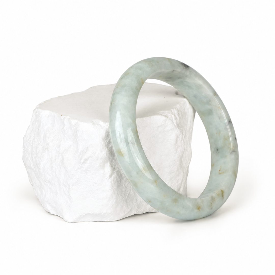 White jadeite bangle with grey and brown markings on a white display rock